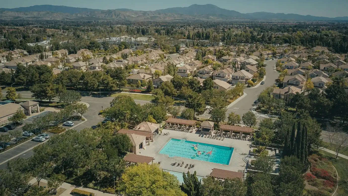 Aerial view of a freeway running through a city with homes, commercial buildings, trees, and rolling hills in the distance.