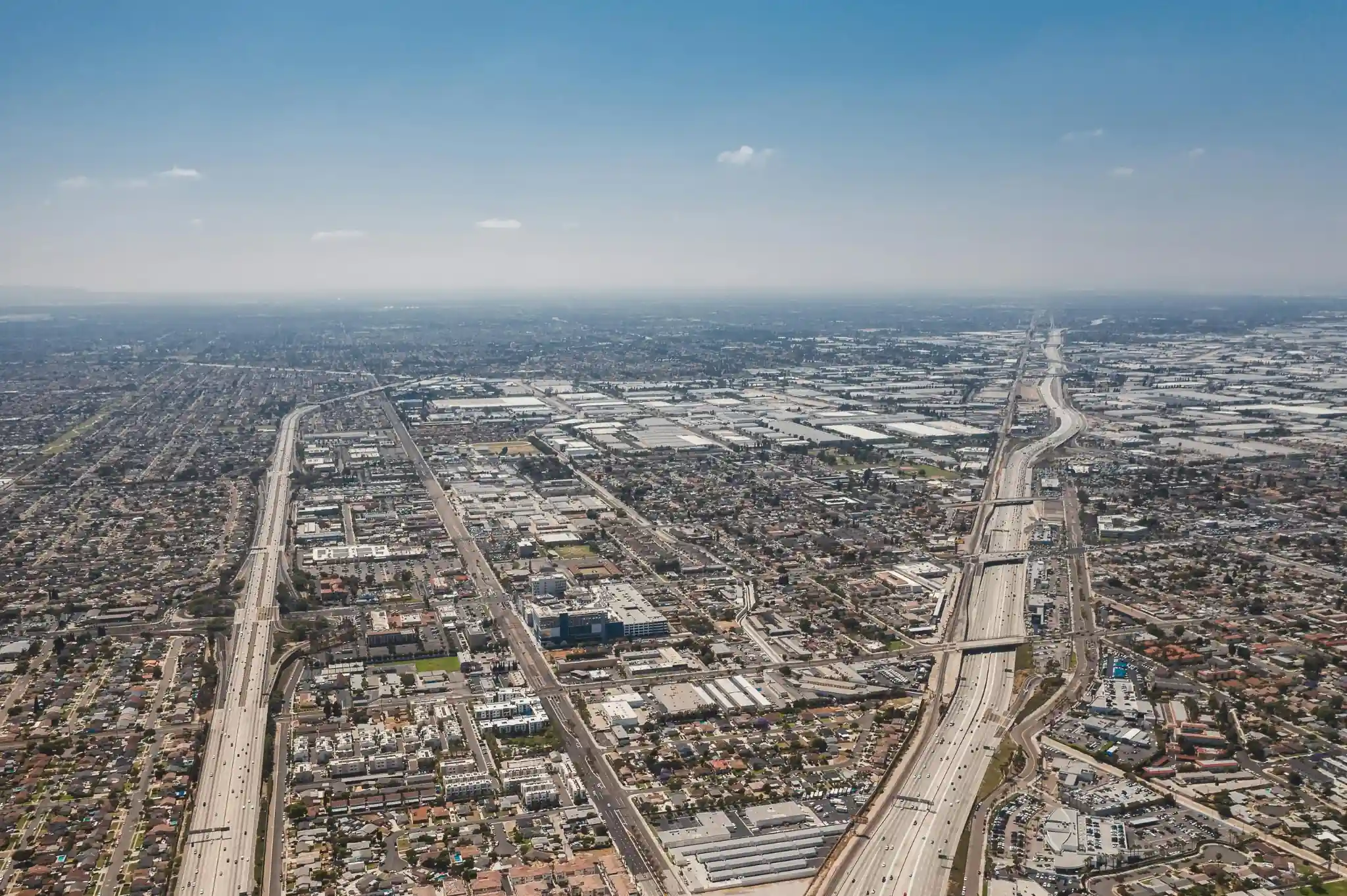 Aerial view of Orange County neighborhoods, freeways, and commercial buildings under a clear blue sky.