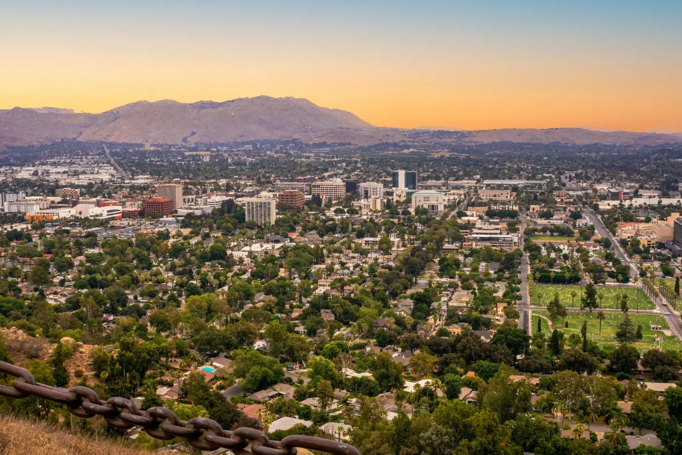 Aerial view of Riverside, California with downtown buildings, neighborhoods, trees, mountains, and sunset